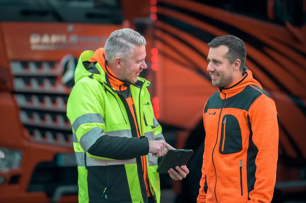 Anställd pratar med chaufför framför orangea lastbilar från MaserFrakt